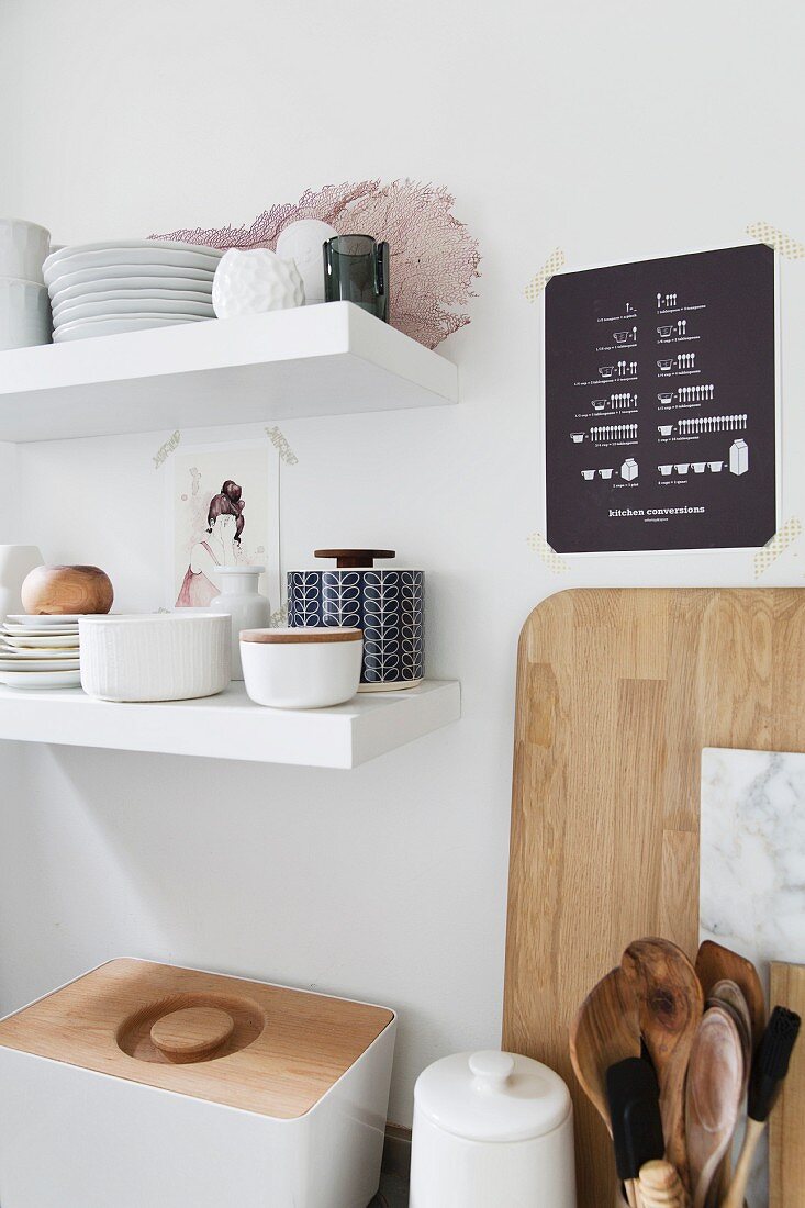 Stacked crockery on white floating shelves above bread bin and kitchen utensils