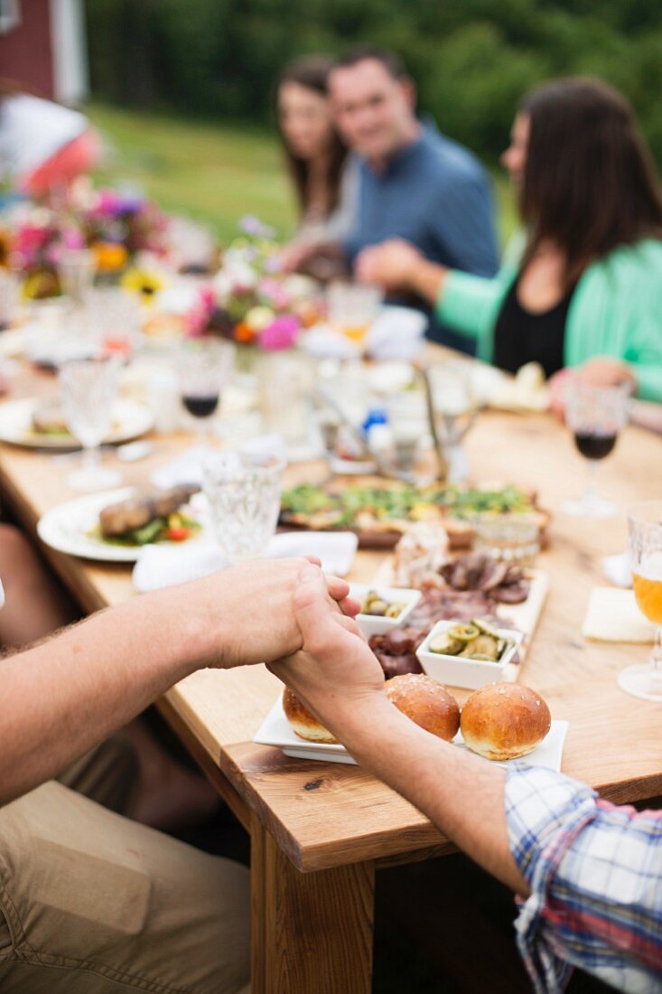 People sitting at a table outside holding hands while saying grace