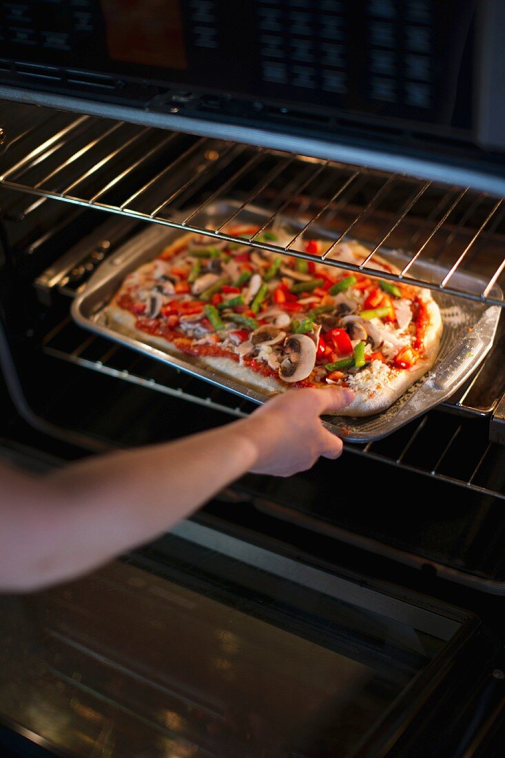 A mushroom pizza being put in the oven
