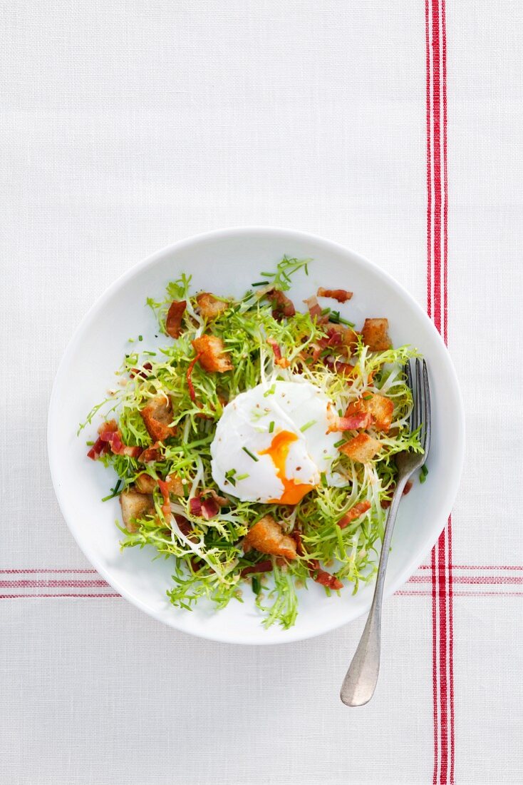 A poached egg on frisee lettuce with bacon and croutons