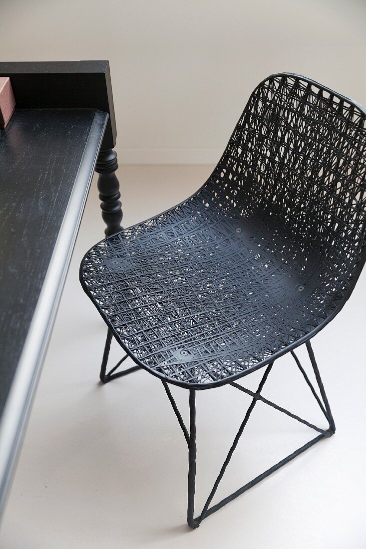 Shell chair with black mesh seat on metal frame next to table