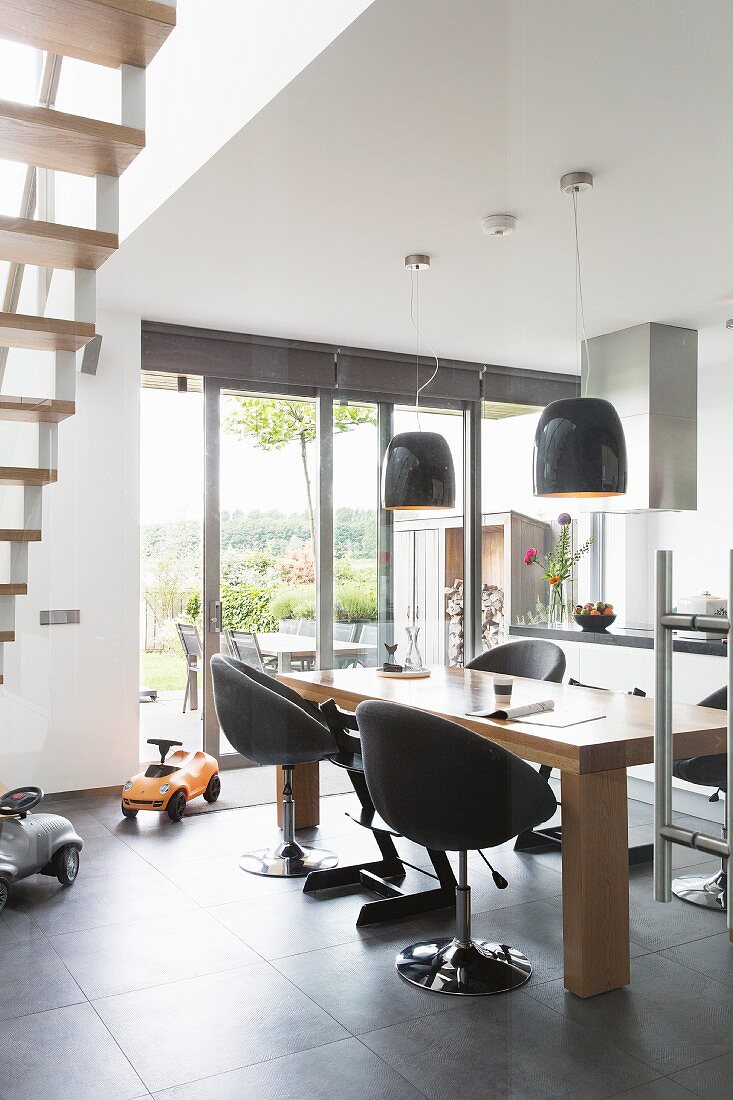 Upholstered swivel chairs at dining table below modern pendant lamps in open-plan kitchen with view of garden