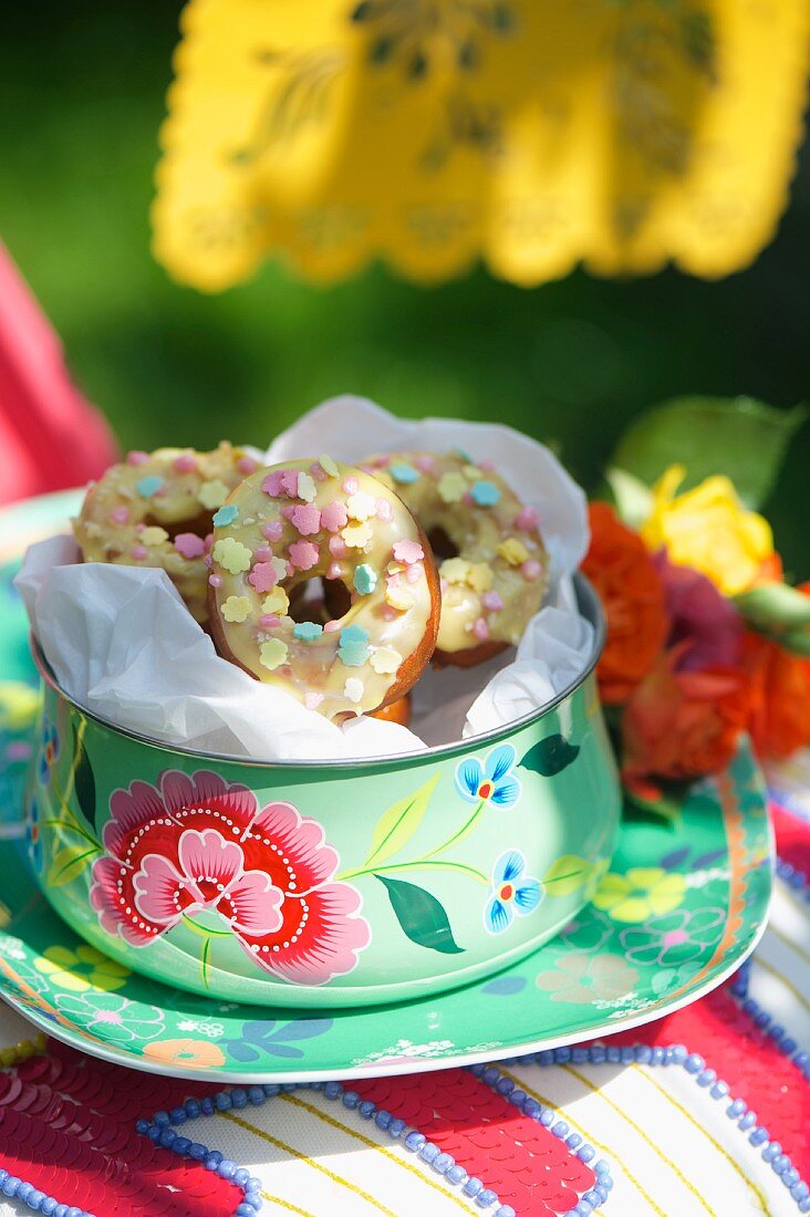Mini-Donuts mit Zuckerglasur in einer bunten Blechdose zum Sommerfest