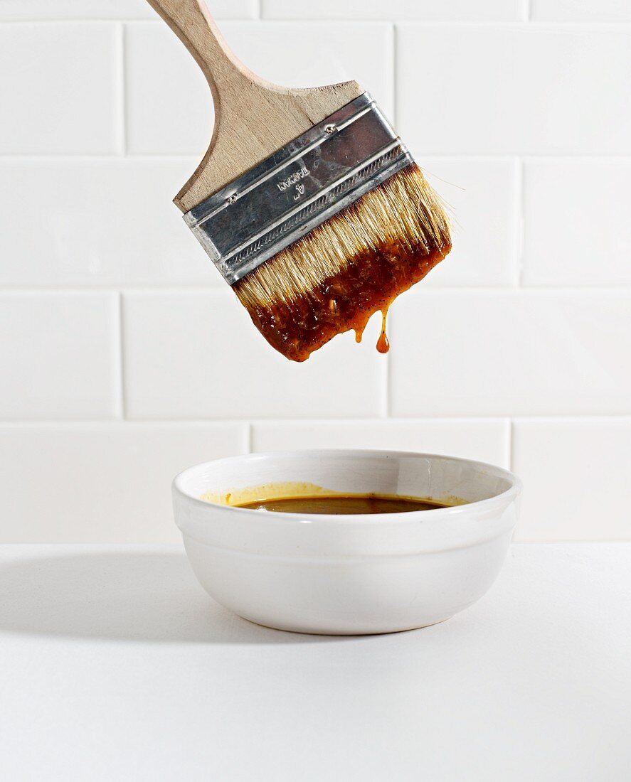 A brush being dipped in a bowl of barbecue sauce