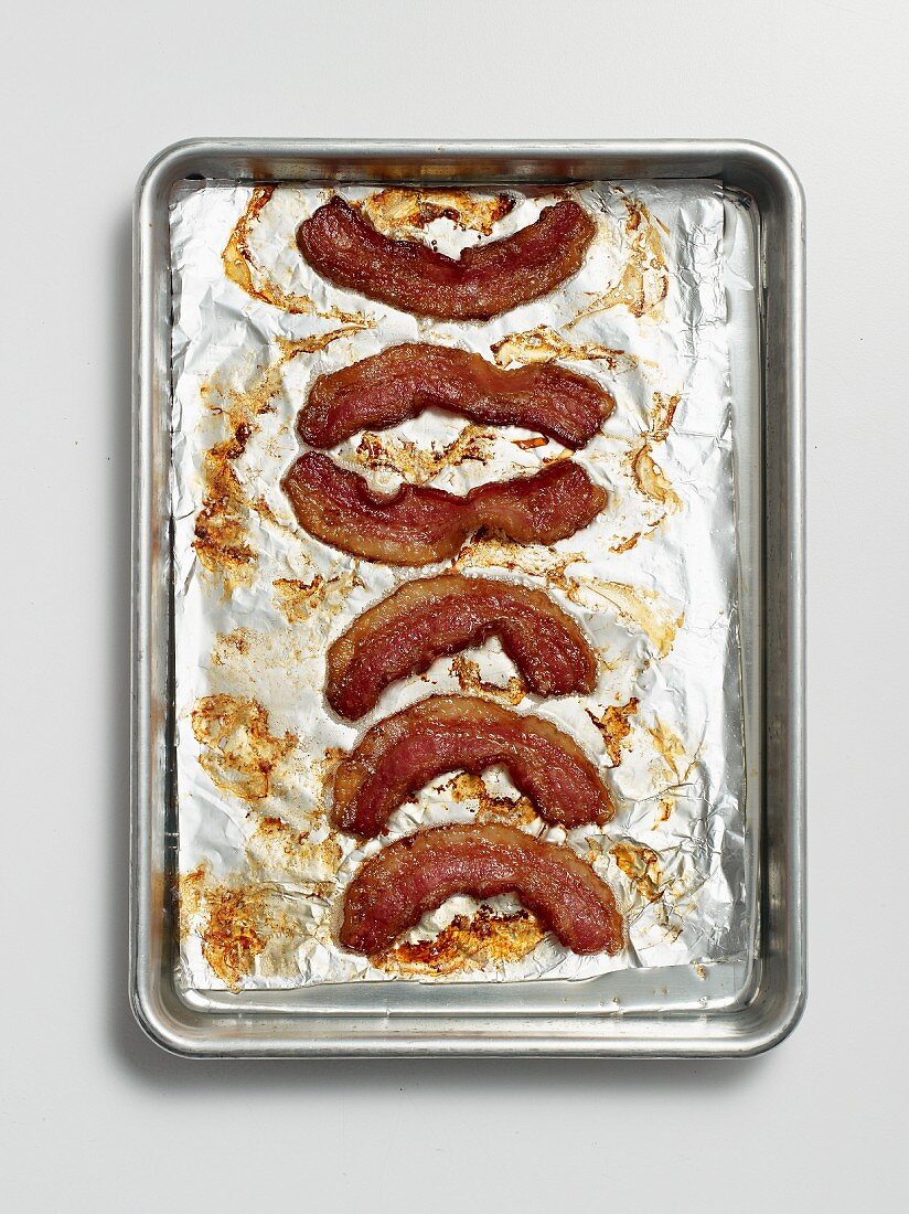Roasted rashers of bacon on a baking tray lined with tin foil