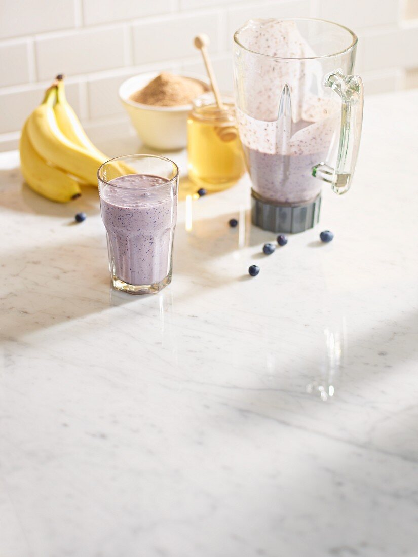 Heidelbeer-Bananenshake im Mixkrug und in einem Glas mit Zucker und Honig