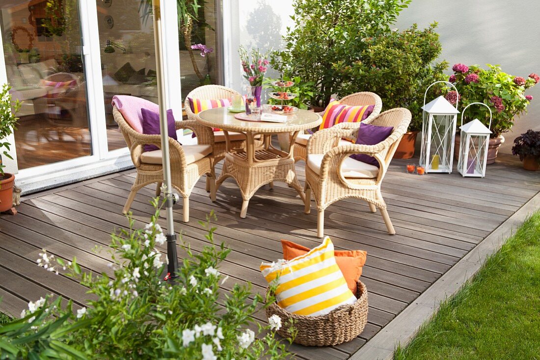 Gemütlicher Sitzplatz mit Rattanmöbeln auf selbstgebauter Holzterrasse, im Vordergrund Korb mit Kissen