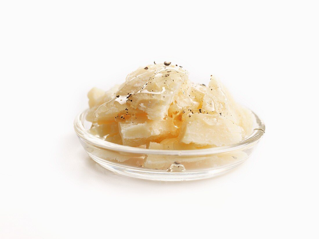 Parmesanstücke mit Honig und Pfeffer im Glasschälchen