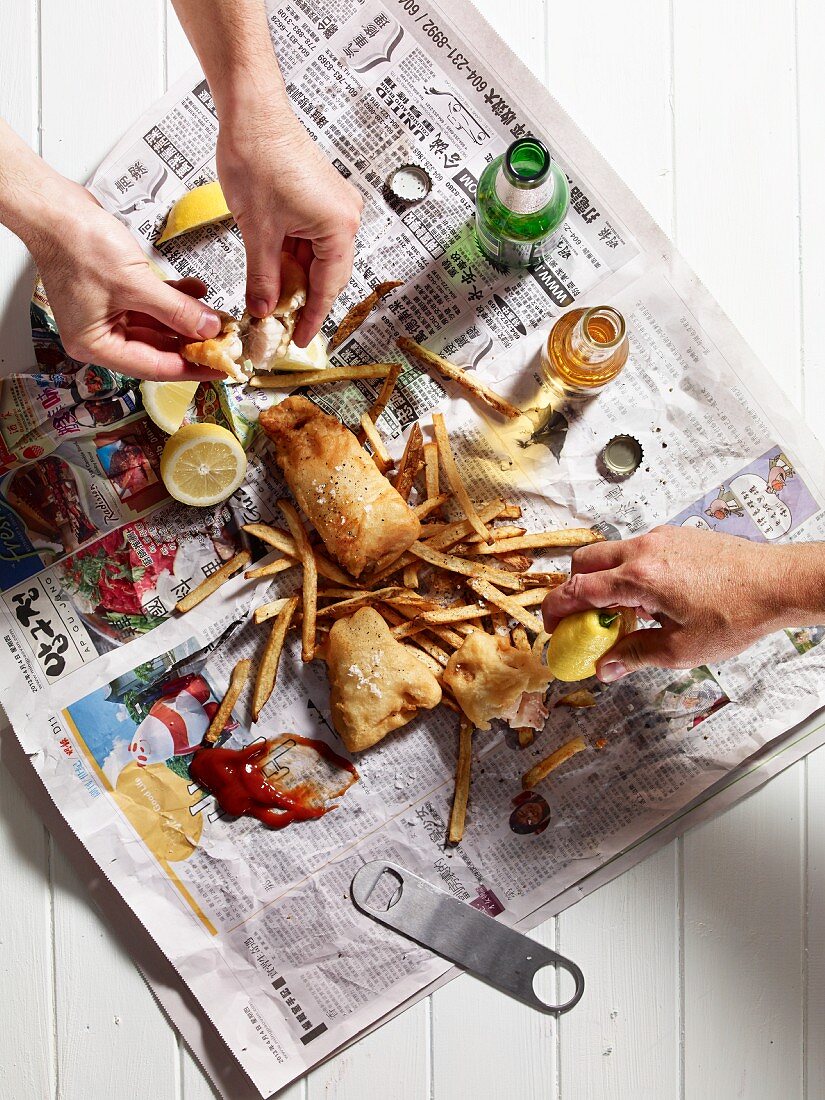 Hands reaching for fish and chips on a piece of newspaper