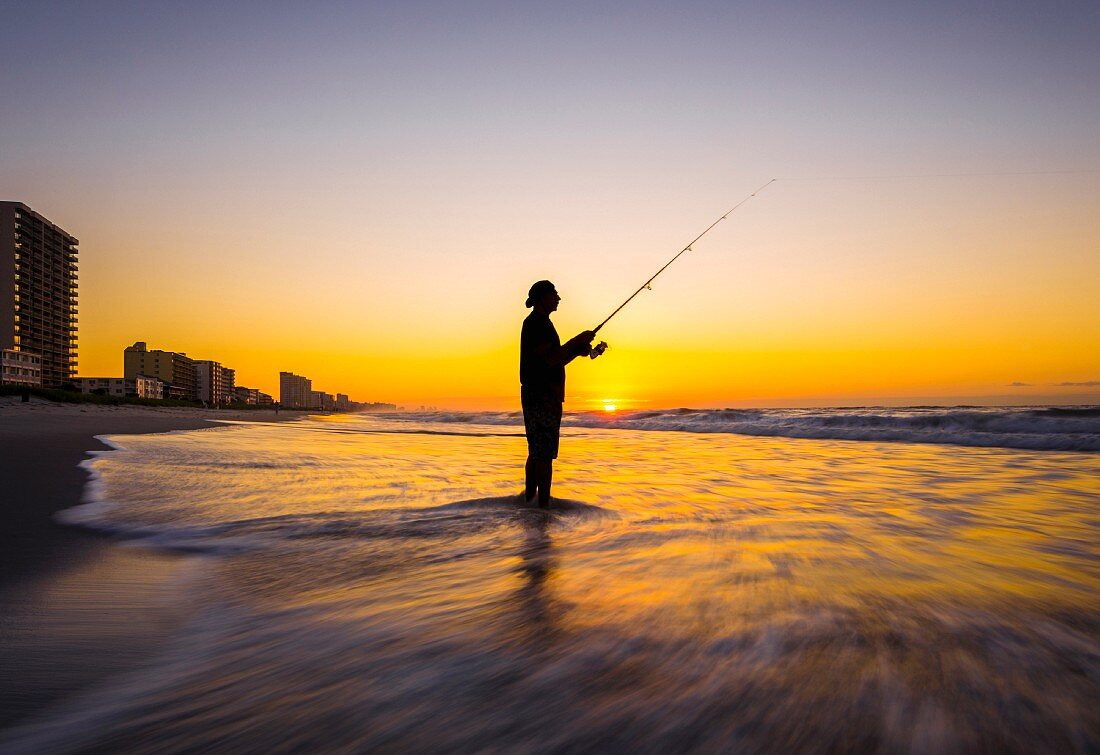A man fishing in the evening sun on a sandy beach