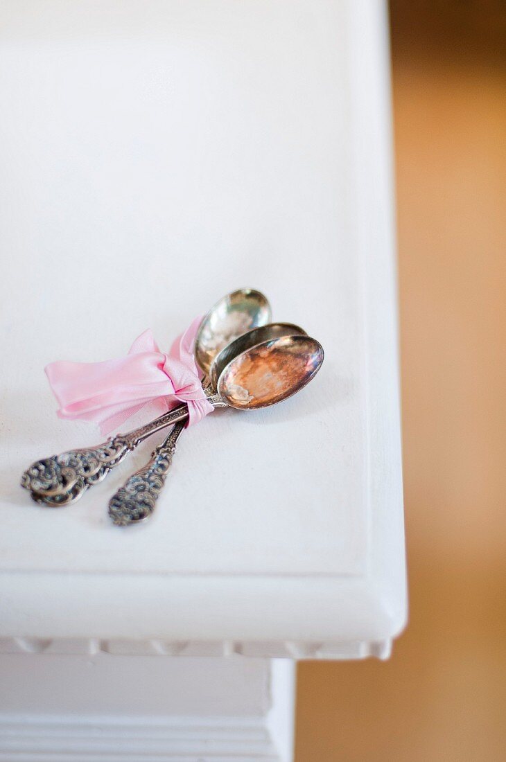 Three antique silver spoons tied with a pink ribbon on a white table