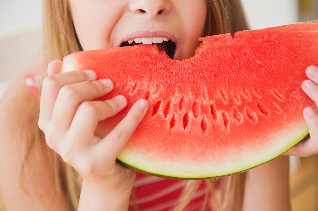 A girl biting into a slice of watermelon