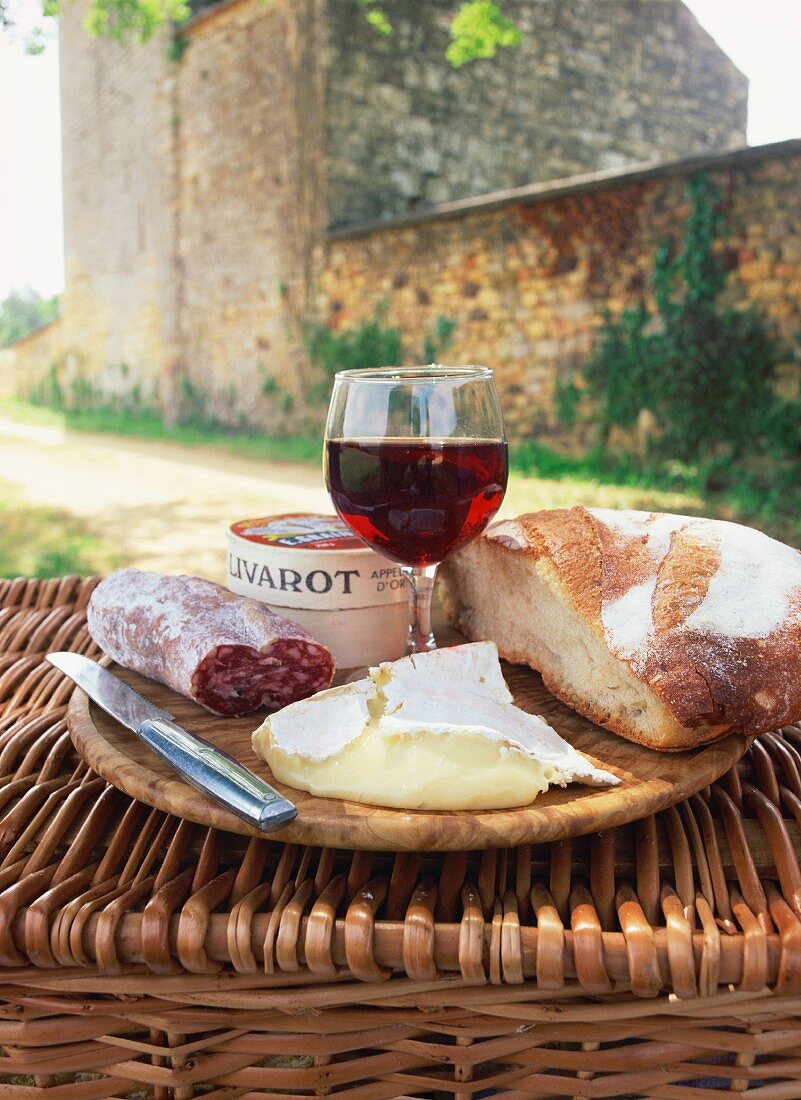 A picnic with bread, red wine, cheese and sausage on top of a wicker basket in the Dordogne, France, Europe