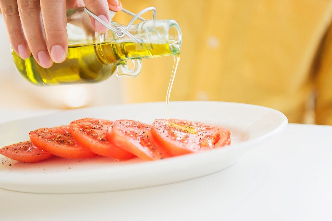 Olivenöl über einen Tomatensalat träufeln
