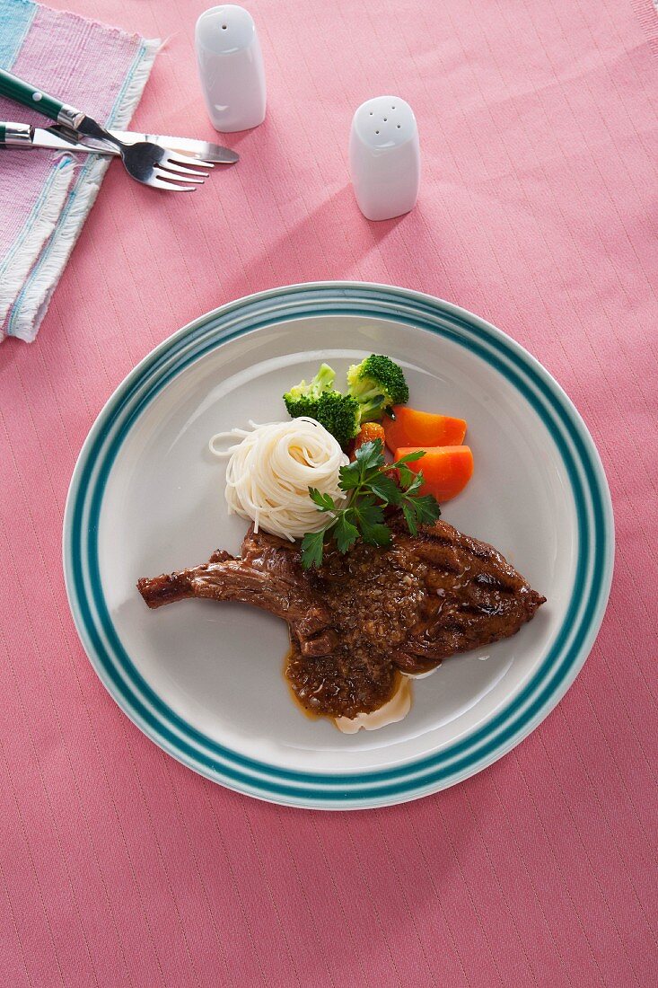 A pork chop with spaghetti, broccoli and carrots