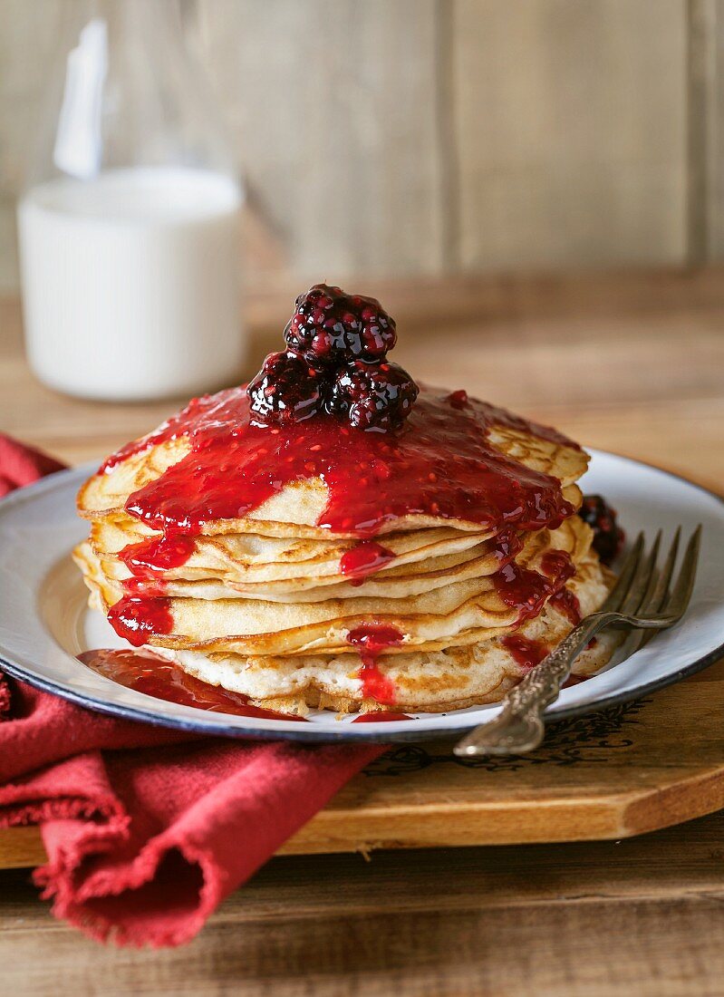 A stack of pancakes topped with blackberry sauce with a bottle of milk in the background