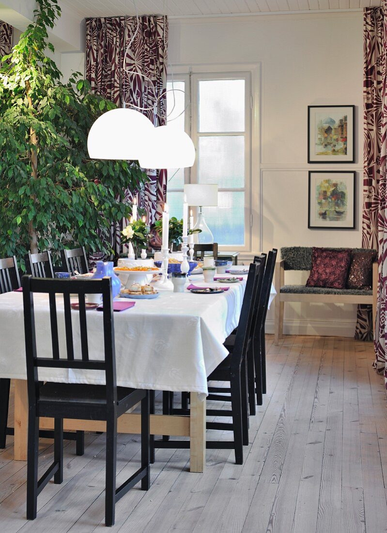 White pendant lamps over table with white tablecloth and black chairs on rustic wooden floor