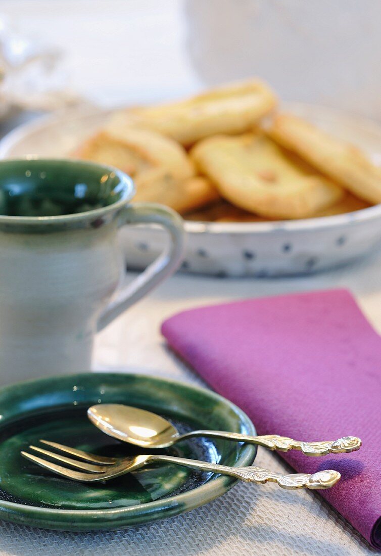 Vintage cutlery on green ceramic plates with dish of pastries in background