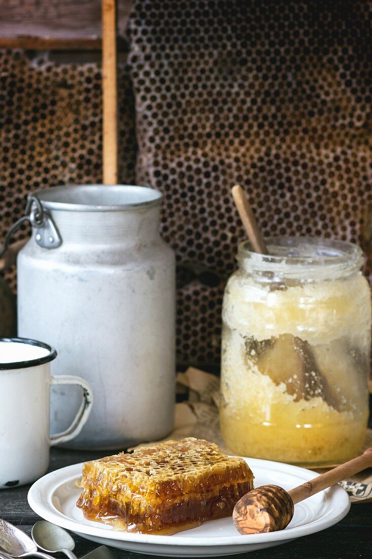 Honeycomb with a honey spoon and a jar of old honey on a old wooden table
