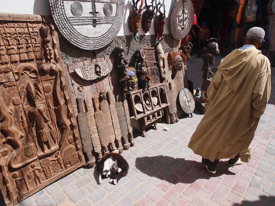 Eine Sonnenanbeterkatze vor Holzkunstwerk in der Medina von Essaouira, Marokko