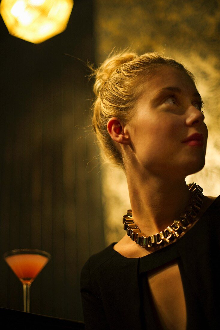 A young woman wearing an evening dress sitting at a bar with a cocktail