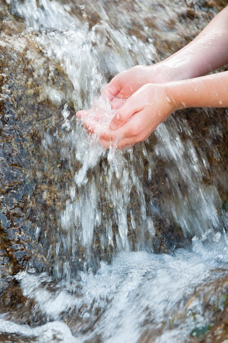 Person holding their hands under the flowing water of a mountain stream