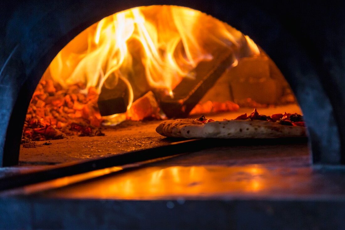 Pizza aus dem brennenden Holzofen ziehen