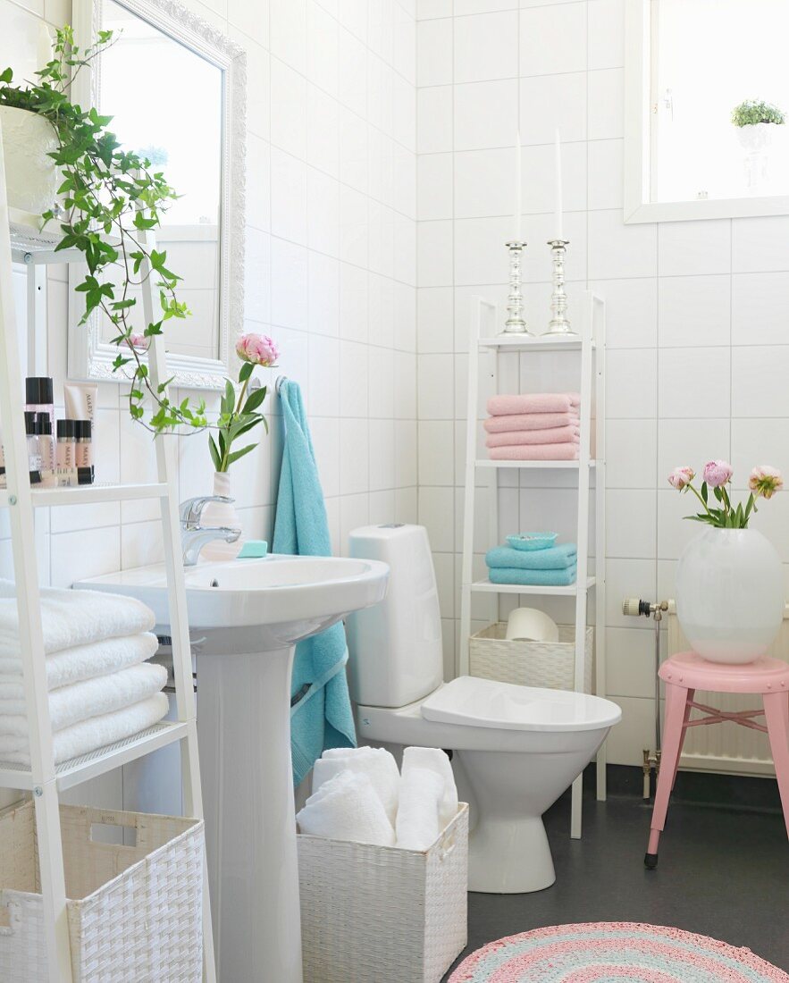 Pedestal sink between shelves of pink and pale blue towels in white-tiled bathroom with romantic atmosphere