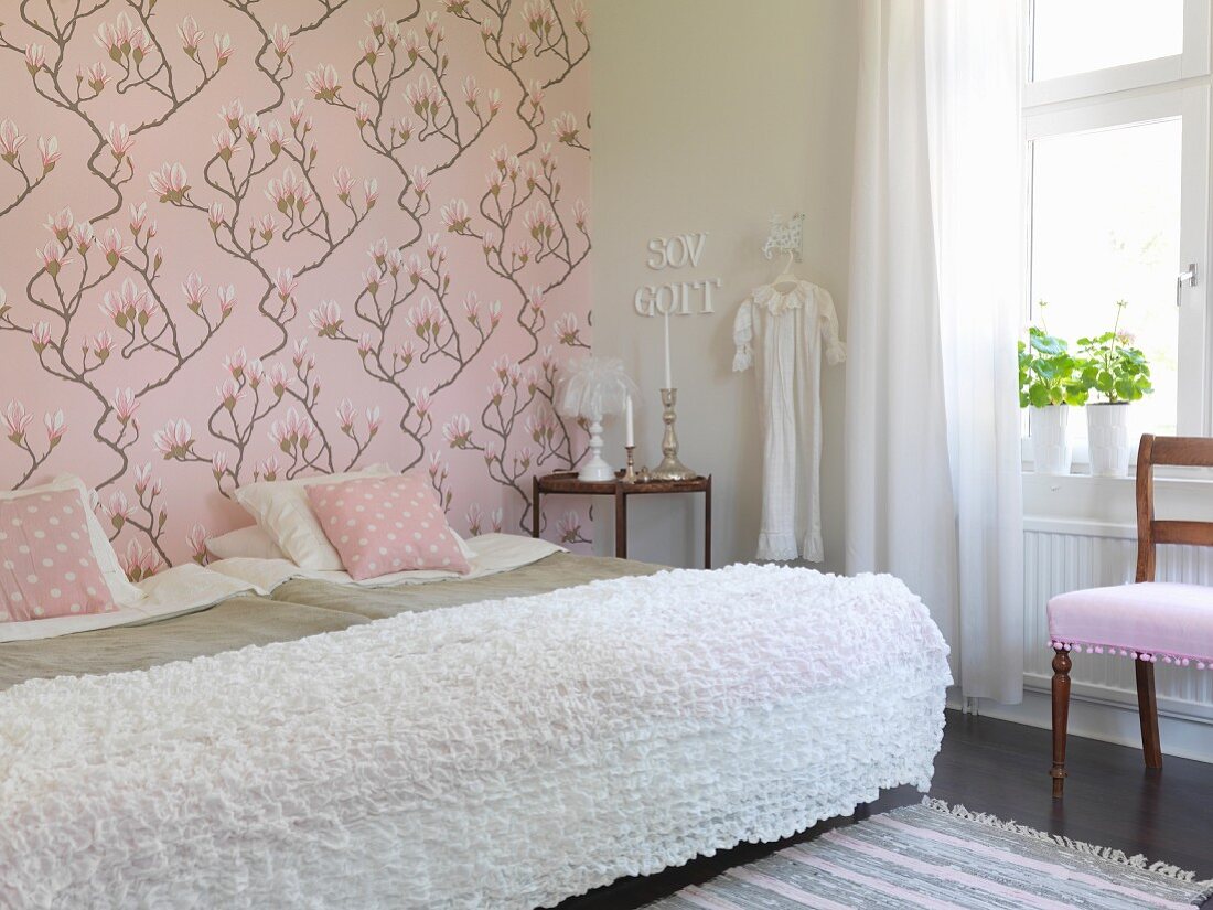 Twin beds pushed together with white blanket in romantic bedroom with pink, magnolia-patterned wallpaper