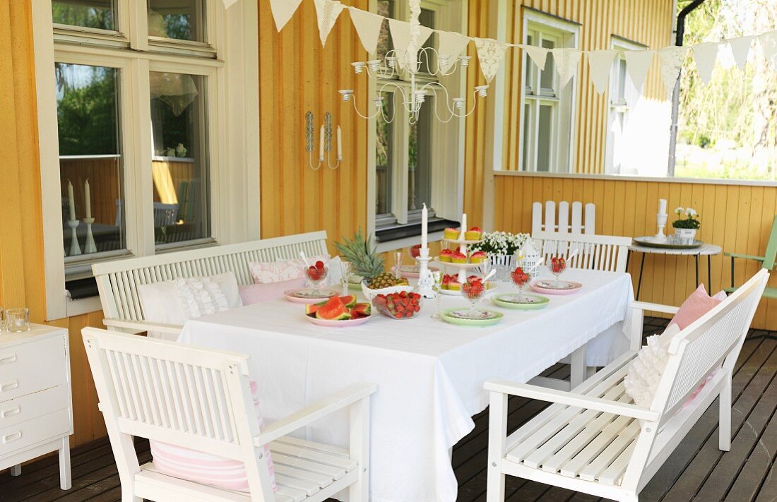 White wooden furniture around set table on veranda of yellow wooden house