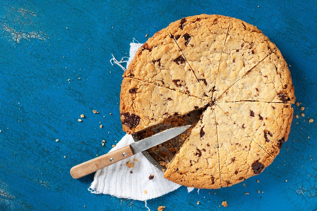 A chocolate chip cookie cake in the tin with a piece missing