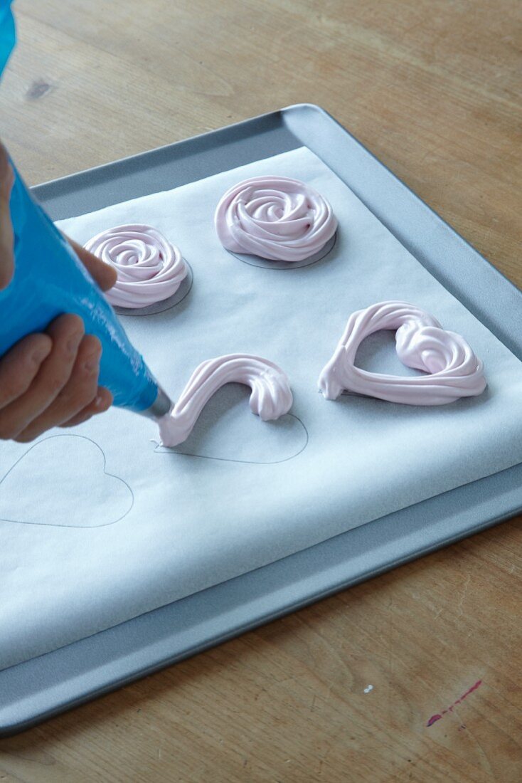 Meringue hearts being piped onto baking paper