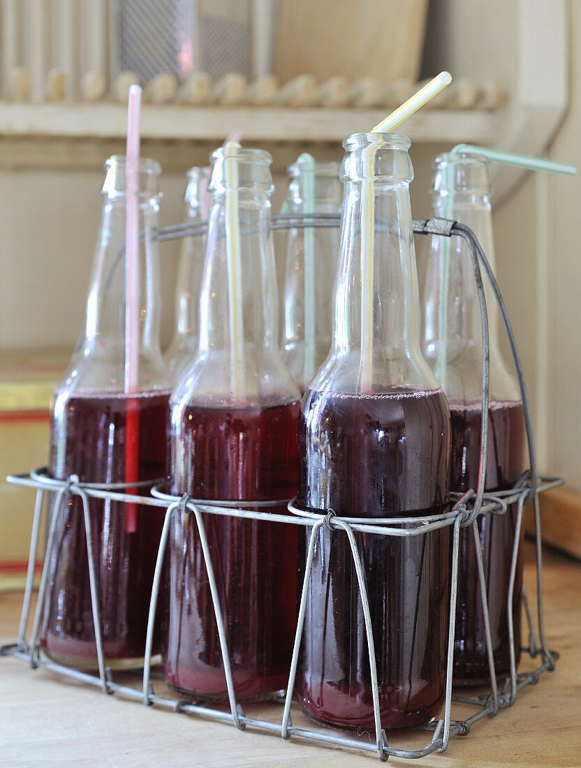 Drinking straws in bottles of cranberry juice in rustic wire bottle carrier