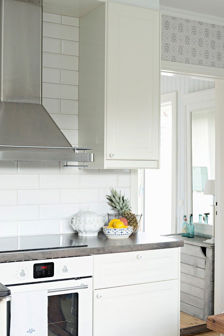 Detail of kitchen counter with white base units and cooker below stainless steel extractor hood