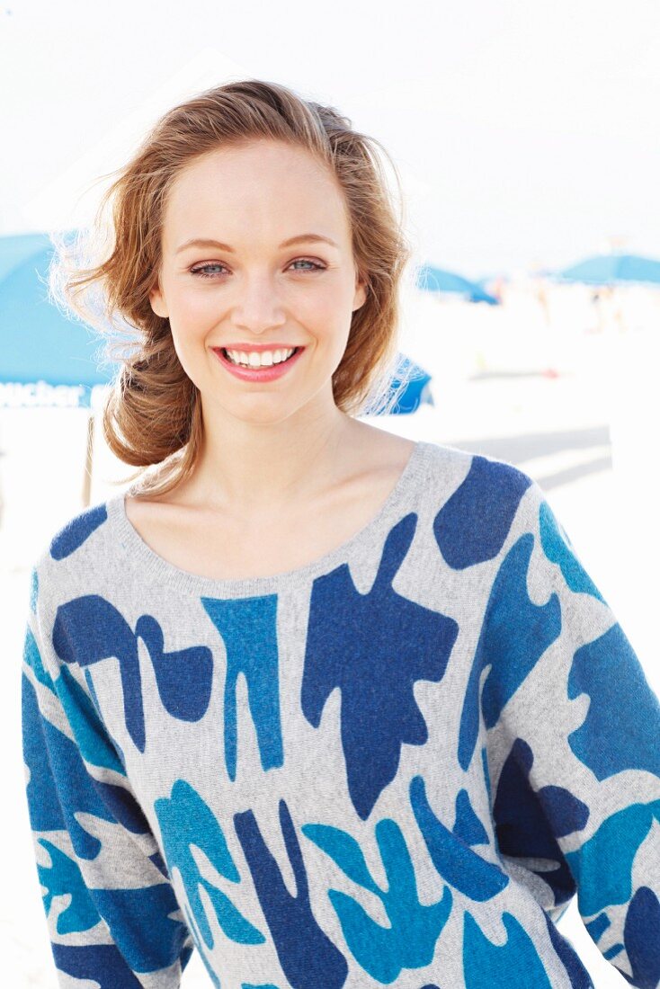 A young blonde woman on the beach wearing a blue patterned jumper