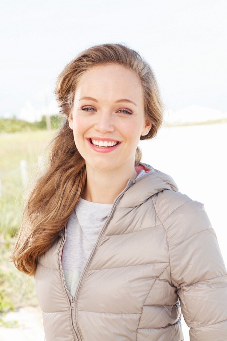 A young blonde woman outside wearing a beige quilted jacket