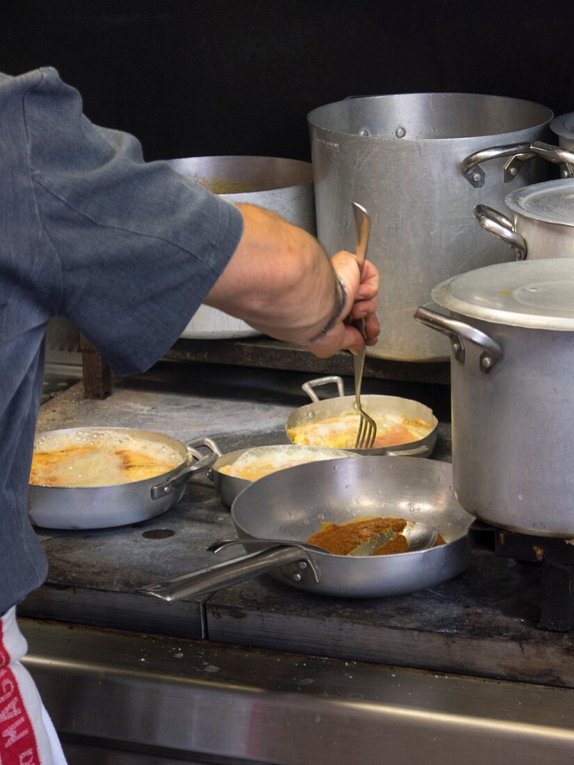 A chef coating chicken breast with breadcrumbs in a commercial kitchen