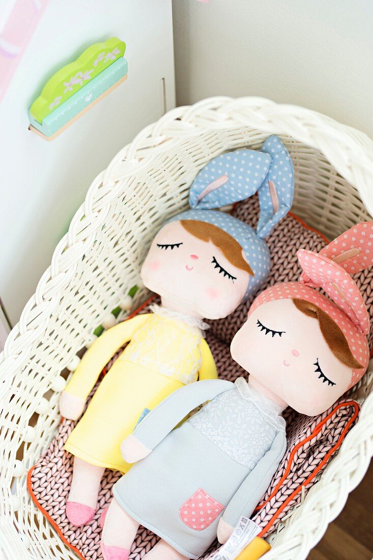 Fabric dolls with sleeping eyes and wearing bunny ears in wicker basket