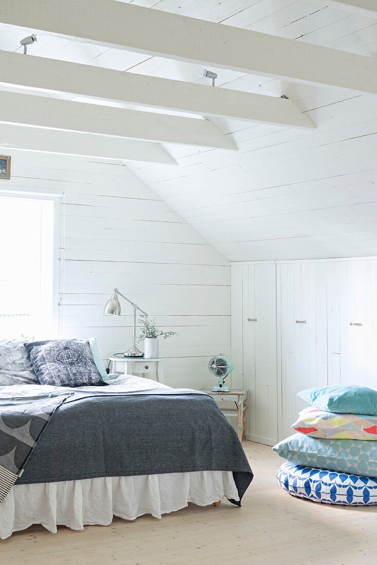 Double bed and stack of cushions in front of fitted wardrobes in wood-clad attic bedroom
