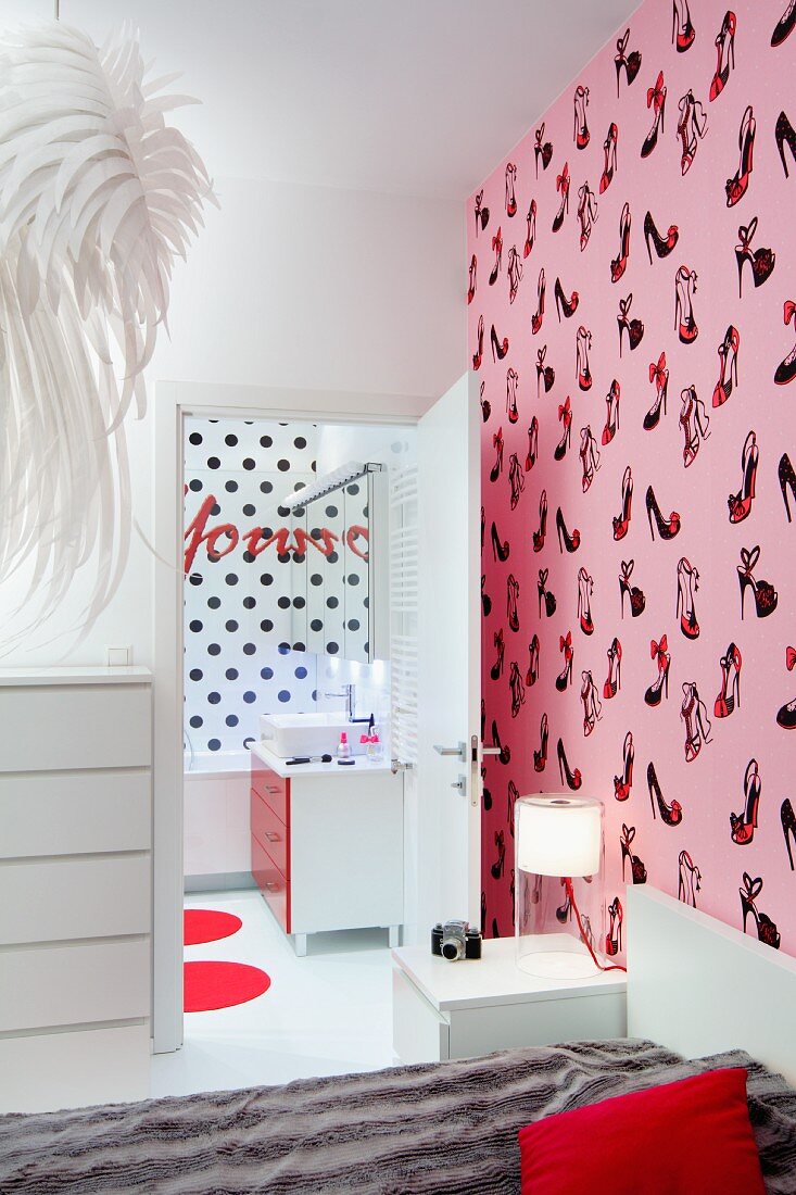 Bett vor rosafarbener Tapete mit Pumps-Motiven, Blick in Bad Ensuite mit schwarz gepunkteter Rückwand