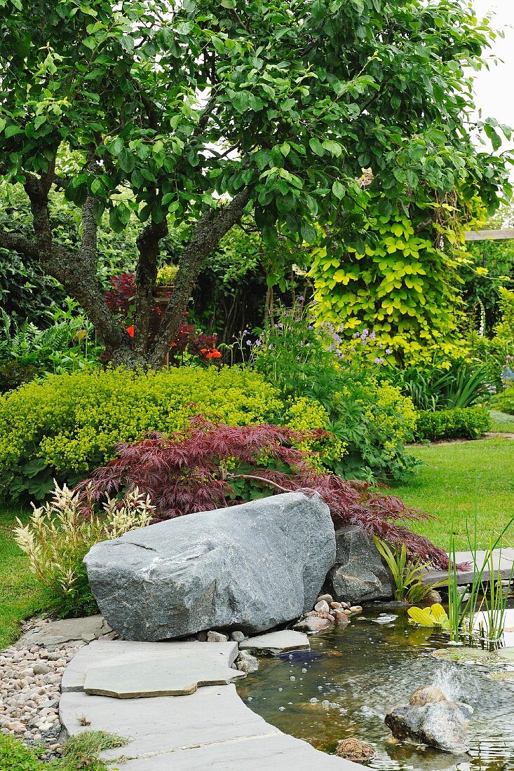 Teich mit Findling am Rand in sommerlichem Garten