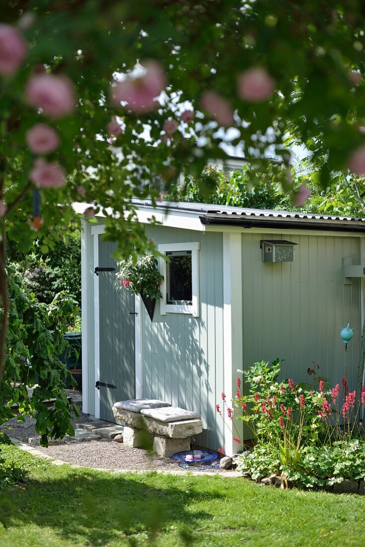 Small shed painted grey and stone bench in summery atmosphere