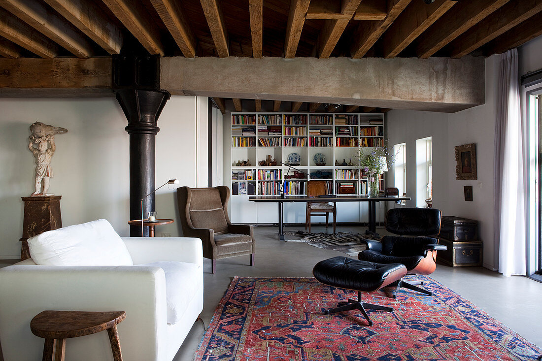 weiße, moderne Couch und Klassiker Lounge Chair auf Orientteppich, im Hintergrund Arbeitsbereich mit Bücherwand