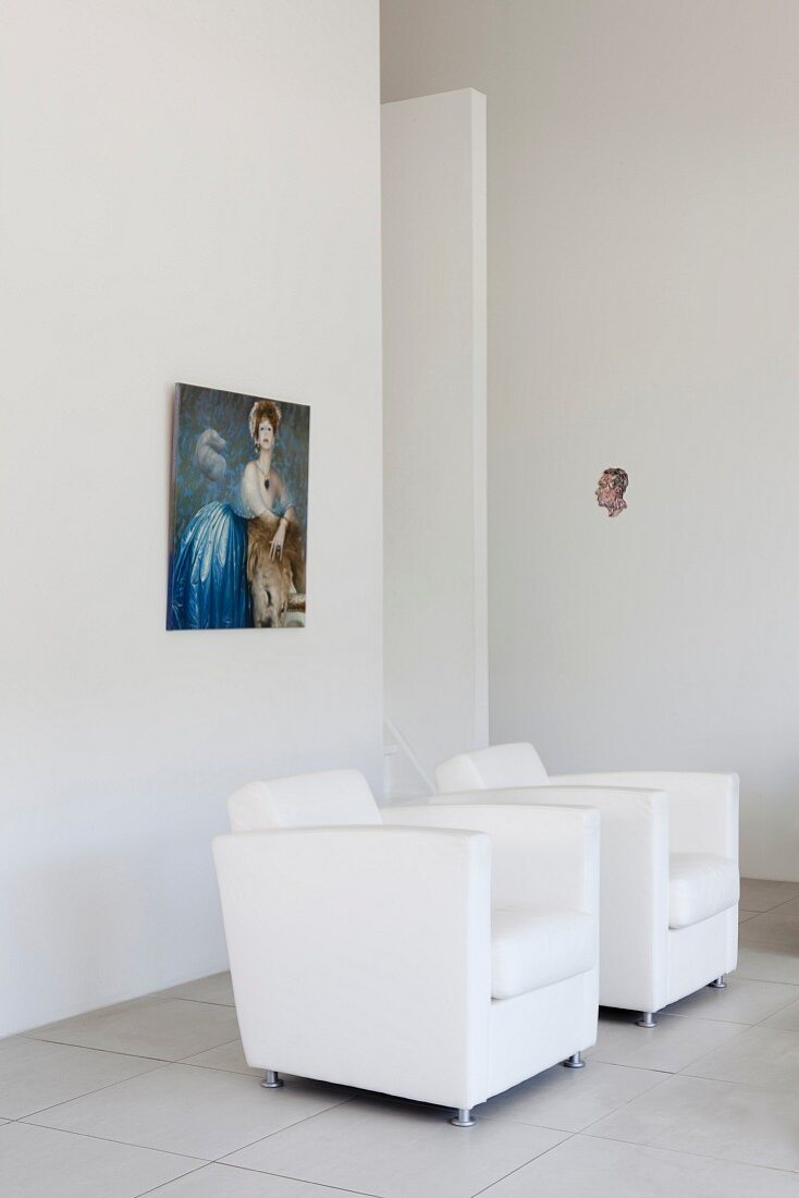weiße Designersessel vor Wand mit aufgehängtem Bild, in minimalistischem Ambiente