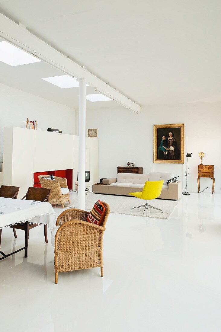 Minimalist loft apartment with wicker chair in dining area and yellow swivel chair and designer sofa in lounge area in background