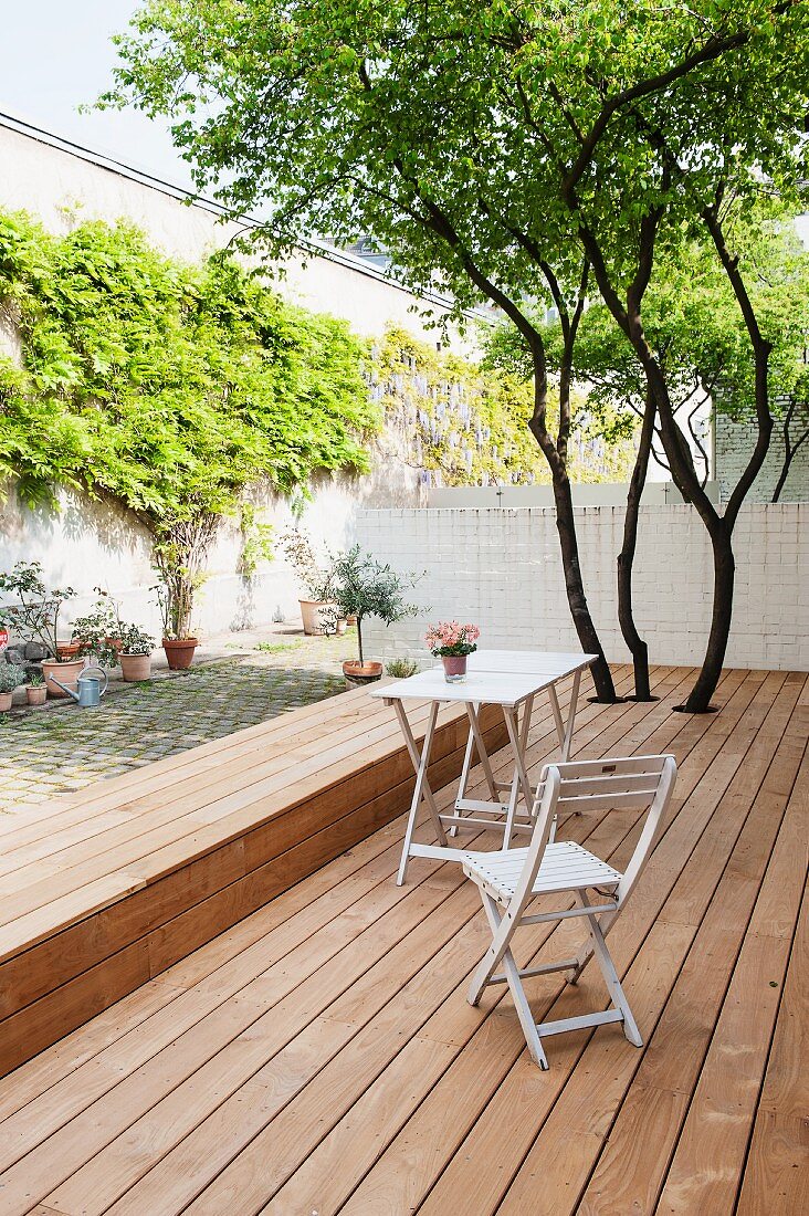 Simple garden chair and table on wooden terrace with integrated bench in courtyard with climber-covered wall