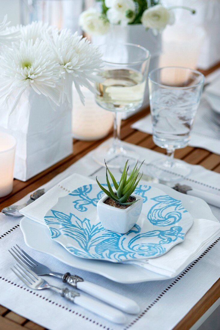 Festive place setting with a white linen place mat and a small decorative succulent plant on a plate