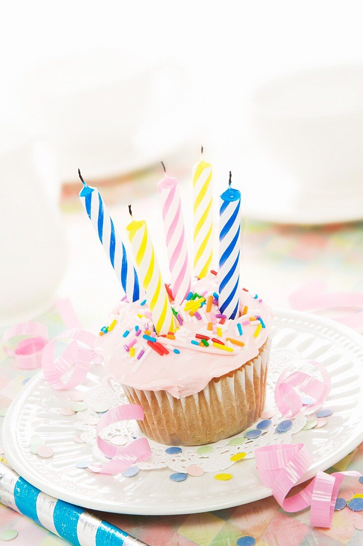 A birthday cupcake with pink frosting and five candles