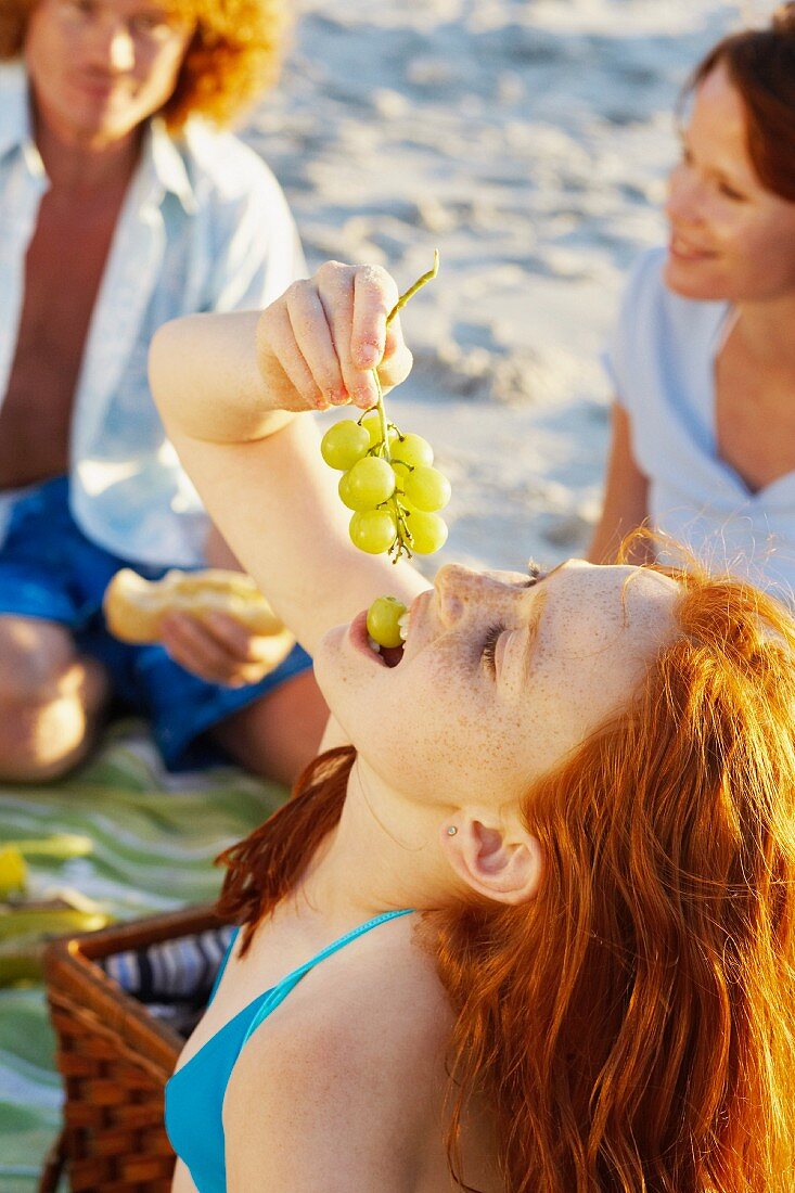 A girl eating grapes at a beach picnic