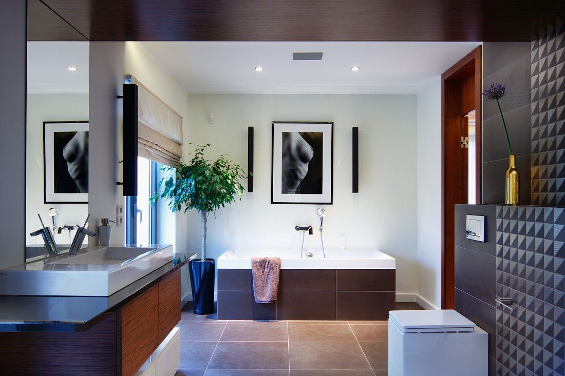 Elegant designer bathroom with brown-tiled wall and ceiling, washstand to one side and bathtub with tiled surround